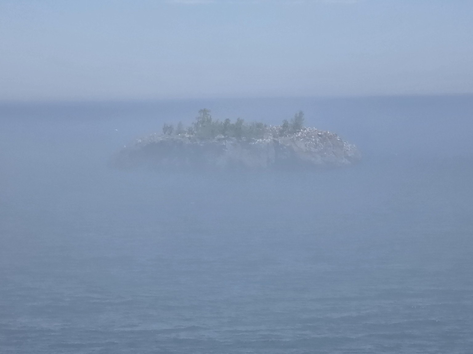 Small rocky Lake Superior island partly obscured by fog