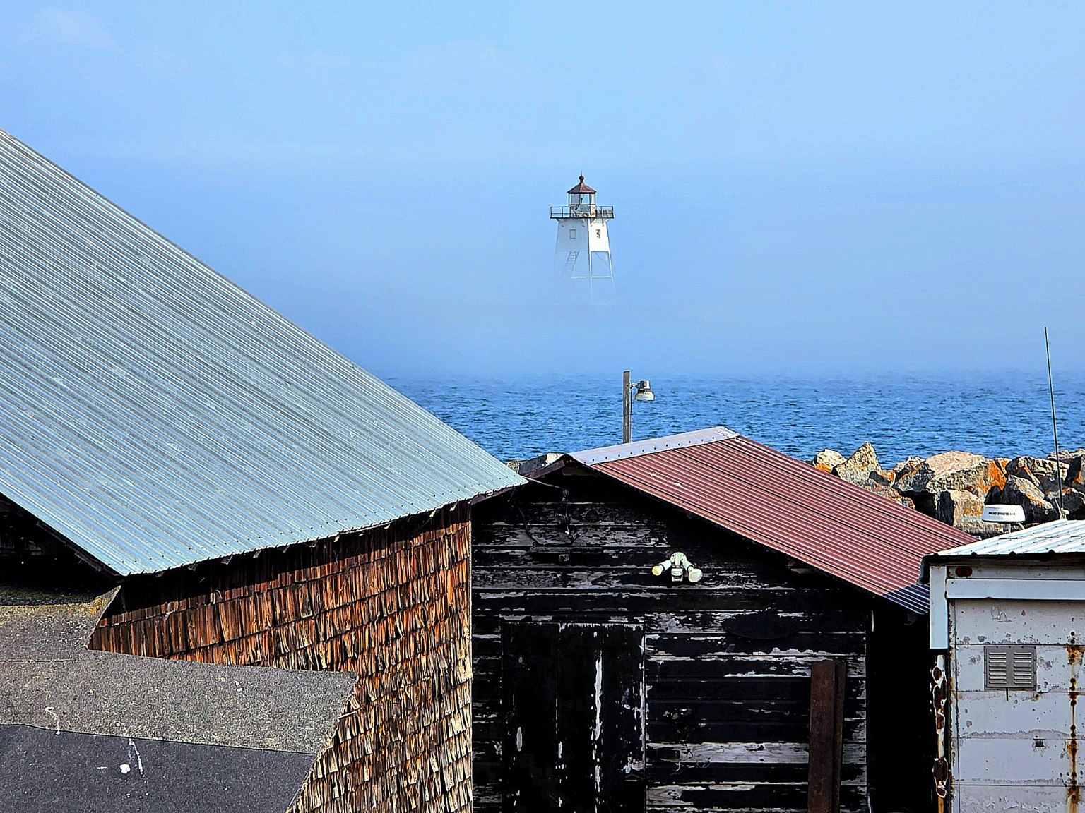 Lighthouse visible through fog beyond historic harbor buildings